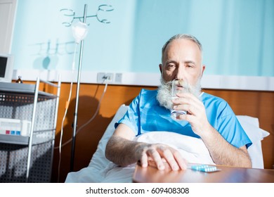 Bearded senior man sitting on hospital bed and taking medicine - Powered by Shutterstock