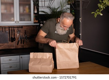 Bearded Senior Man Unpacking Shopping Bags With Food In Kitchen.