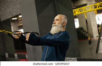 Bearded Senior Sportsman Training With Trx Resistance Bands In Gym.