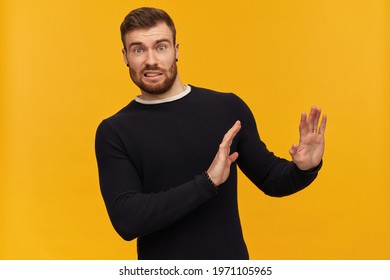 Bearded Shocked Guy, Skeptical Looking Man With Brunette Hair. Has Piercing. Wearing Black Sweater. Pushes Arms Away, Reject Gesture. Watching At The Camera, Isolated Over Yellow Background