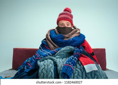 Bearded sick man with flue sitting on sofa at home or studio covered with knitted warm clothes. Illness, influenza, pain concept. Relaxation at Home. Healthcare Concepts. - Shutterstock ID 1182460027