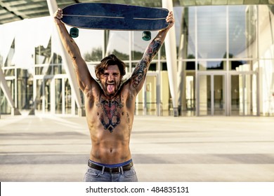 Bearded skater with tattoos holding longboard outside of conference center - Muscular man showing body in urban area - Rebel against system concept - Vintage editing - Warm filter  - Shutterstock ID 484835131