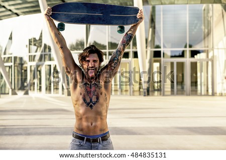 Bearded skater with tattoos holding longboard outside of conference center - Muscular man showing body in urban area - Rebel against system concept - Vintage editing - Warm filter 