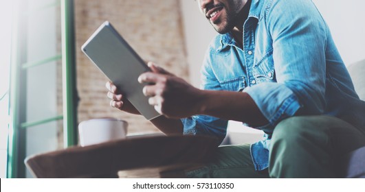 Bearded smiling African man using tablet for video conversation while relaxing on sofa in modern office.Concept of young business people working at home.Blurred background.Horizontal wide - Powered by Shutterstock