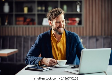 Bearded smiling Caucasian freelancer sitting in cafe, drinking fresh coffee and using lapotp. - Powered by Shutterstock