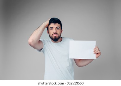 The Bearded Student In A White T-shirt Holding A Blank Sheet Of Paper. 
Isolated On A Light Background
 .