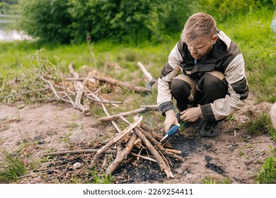 Bearded survivalist male in raincoat starting fire using gas lighter on bank of river for cooking and warming in evening before sunset. Concept of exploration, travel and adventure. - Powered by Shutterstock