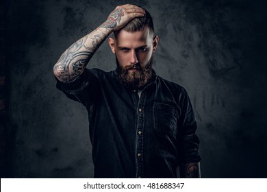 The bearded tattooed male holding head on grey background.