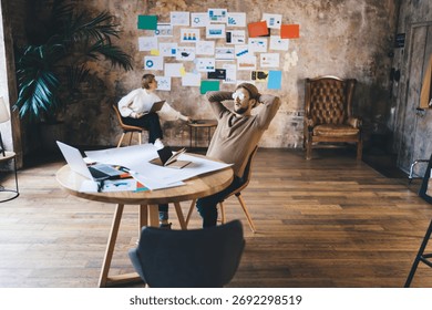 Bearded tech freelancer leans back during laptop planning session, contemplating digital strategy results and visualizing progress in flexible remote startup workspace.