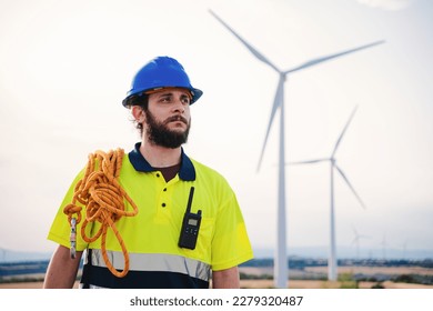 Bearded technician engineer of windmill and renewable energy industry working and looking the turbine to reapir and fix the problems wearing helmet an saftery vest. Electricty power concept. High