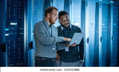 Bearded IT Technician in Glasses with Laptop Computer and Black Male Engineer Colleague are Using Laptop in Data Center while Working Next to Server Racks Running Diagnostics or Doing Maintenance Work - Powered by Shutterstock