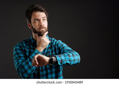 Bearded White Puzzled Man Looking Upward While Using Wristwatch Isolated Over Black Background