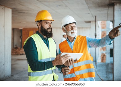 A bearded worker in a yellow hard hat and a senior manager in a white hard hat examine site developments, both clad in reflective vests, amidst an active construction environment. - Powered by Shutterstock