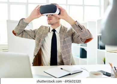 Bearded young interior designer using VR headset in order to work with 3d visualization while carrying out project at modern office with panoramic windows - Powered by Shutterstock