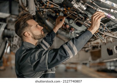 Bearded young man aviation mechanic checking aircraft components while working in repair station