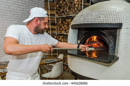 Bearded Young Man Check On Pizza In Wood Fired Oven