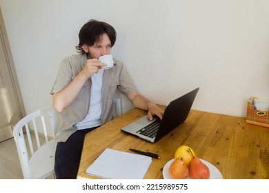 A Bearded Young Man Drinks Coffee Without Looking Up From Work. Remote Work Concept. Copy Space. 