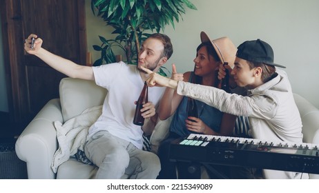 Bearded Young Man Is Holding Smartphone And Taking Selfie With His Friends Musicians Holding Beer Bottles. Friendship, Creative People, Modern Technology And Fun Concept.