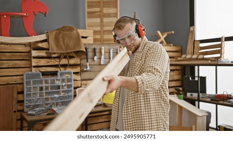 A bearded young man inspects a wooden plank in a well-organized carpentry workshop, wearing protective eyewear and earmuffs. - Powered by Shutterstock