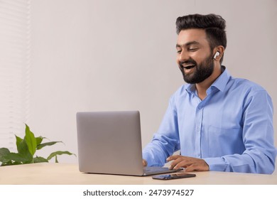 A BEARDED YOUNG MAN LAUGHING WHILE VIDEO CONFERENCING IN OFFICE