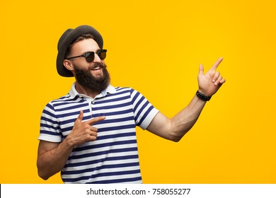 Bearded young man in striped t-shirt and sunglasses pointing away and smiling on orange.  - Shutterstock ID 758055277
