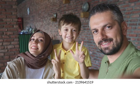 Bearded Young Man With Turbaned Wife And Son Talking To Loved Ones On Video Call With Mobile Phone Camera. Happy Family Waving To Their Loved Ones In The Photo.Frontal Phone Camera View.