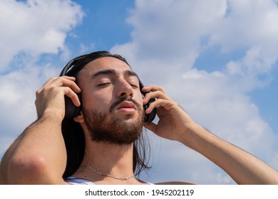 bearded young man with wireless headphones with the sky in the background, reflecting on life, meditating. with eyes closed. surround sound.