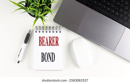 Bearer bond written on a notepad with a pen, laptop, and plant on white desk . 