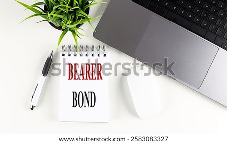 Bearer bond written on a notepad with a pen, laptop, and plant on white desk . 