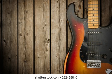 A beat up, dirty and road-worn old vintage electric guitar body against a natural wood-grain boards background.