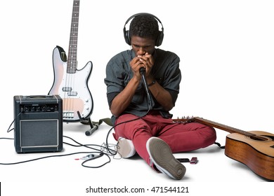 Beatboxer on the floor makes sounds in the microphone in his hands connected to the black amp. Musician in headphones rehearses for his future concert.