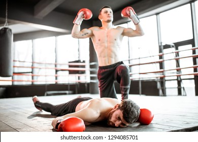 Beaten boxer lying knocked out on the boxing ring with strong man winner above - Powered by Shutterstock