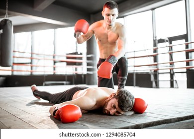 Beaten boxer lying knocked out on the boxing ring with strong man winner above - Powered by Shutterstock