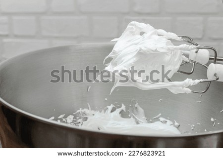 Beaten egg whites with sugar for Meringue in a mixing bowl with an electric hand whisk. Cooking process with kitchen utensils.
