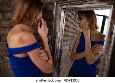 Beaten young woman victim of domestic violence and abuse stands near mirror and views bruises and wounds on her bloody face. concept of domestic violence, sexual violence and cruelty.