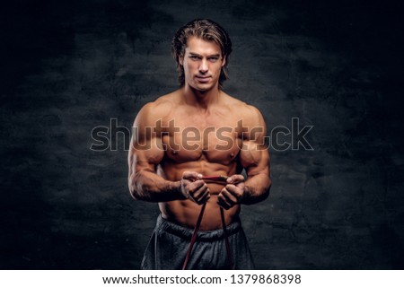 Beatiful smiling bodybuilder is doing exercises with rubber. There is dark background.