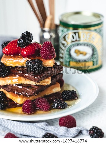 Beatiful stack of chocolate and plain waffles with forest fruit and covered in golden syrup