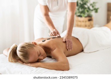 Beatiful woman is enjoying relaxing back massage in cosmetology spa centre. The masseuse applies lava stones to the spine. - Powered by Shutterstock
