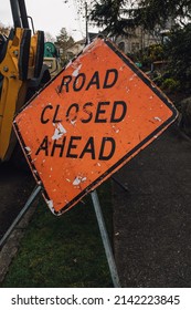 Beat-up, rundown orange Road Closed Ahead warning sign