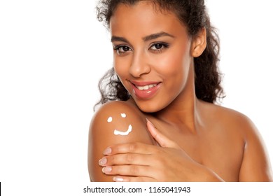 Beauiful dark skinned woman applying body lotion on white background