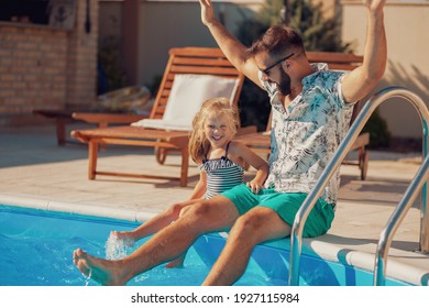 Beauitful cheerful father and daughter sitting at the edge of a swimming pool and having fun outdoors on a hot sunny summer day - Powered by Shutterstock