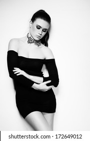 Beautfiul sexy woman in a glamorous off the shoulder black dress and bow tie posing seductively with downcast eyes on white