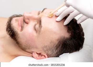 Beautician Applies Wax Between Male Eyebrows Before The Procedure Of Waxing In The Beauty Salon.