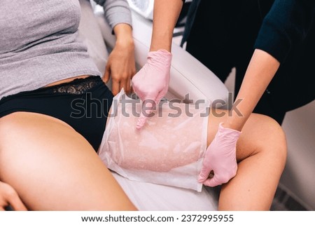 Beautician applying antifreeze membrane before a cryolipolysis procedure on her client's thigh to reduce fat.