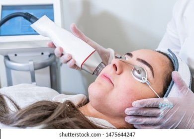 Beautician applying radio frequency microneedling handpiece to a woman's face for skin tightening treatments at a beauty clinic.