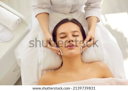 Beautician at beauty center removing makeup with cotton discs, cleaning skin before facial massage or rejuvenating detox mask, applying lotion or chemical peel for beautiful perfect bright complexion