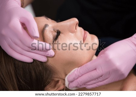 Beautician in a beauty salon holds a cotton pad with which he cleans the face of a woman. Skin care and rejuvenation procedures.	