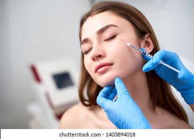 Beautician doctor with botulinum toxin syringe making injection to to remove crow's feet. Cheek volume enhance mesotherapy. Anti-aging treatment and face lift in cosmetology clinic.