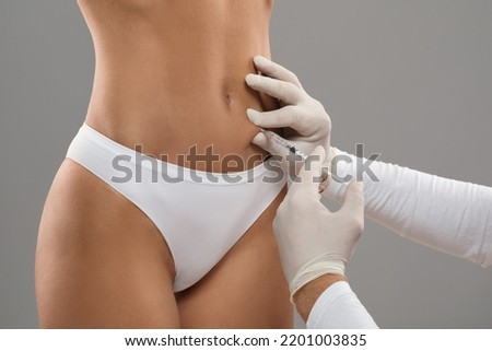 Beautician Doctor Wearing Gloves Making Beauty Injection To Female Patient Belly, Unrecognizable Young Woman In Underwear Getting Lipolysis Treatment For Slimming, Standing On Grey Background