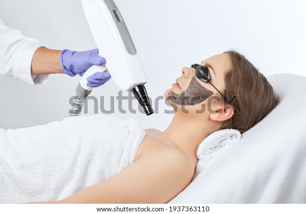 Beautician does laser carbon peeling procedure on\
the problem skin against acne of a young beautiful girl.\
Cosmetology and professional skin\
care.